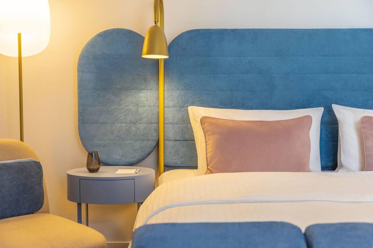 A bedroom with a blue headboard, a bedside table with a lamp, and a bed with pillows.