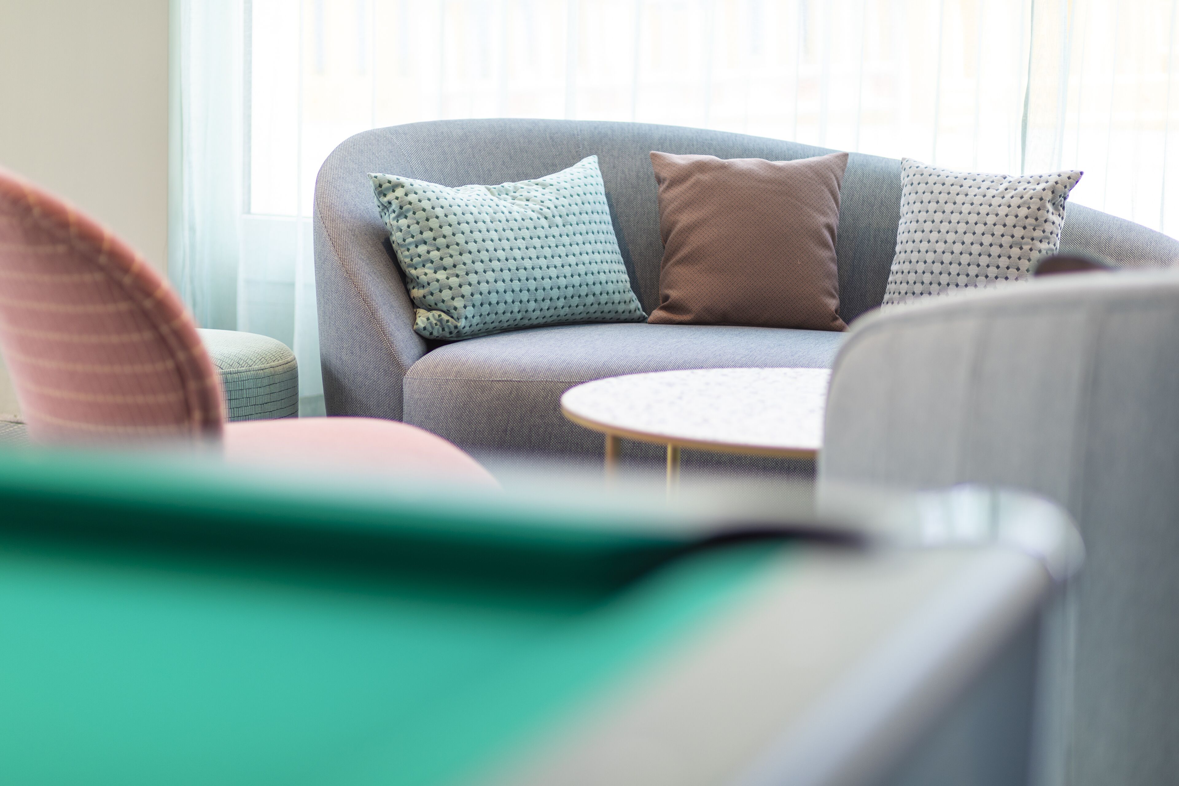 Ein modernes Wohnzimmer mit einem grauen Sofa, gemusterten Kissen und einem kleinen runden Tisch.