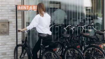 Una persona apoyada en una bicicleta frente a un edificio con un letrero que dice 'RENT A BIKE'.