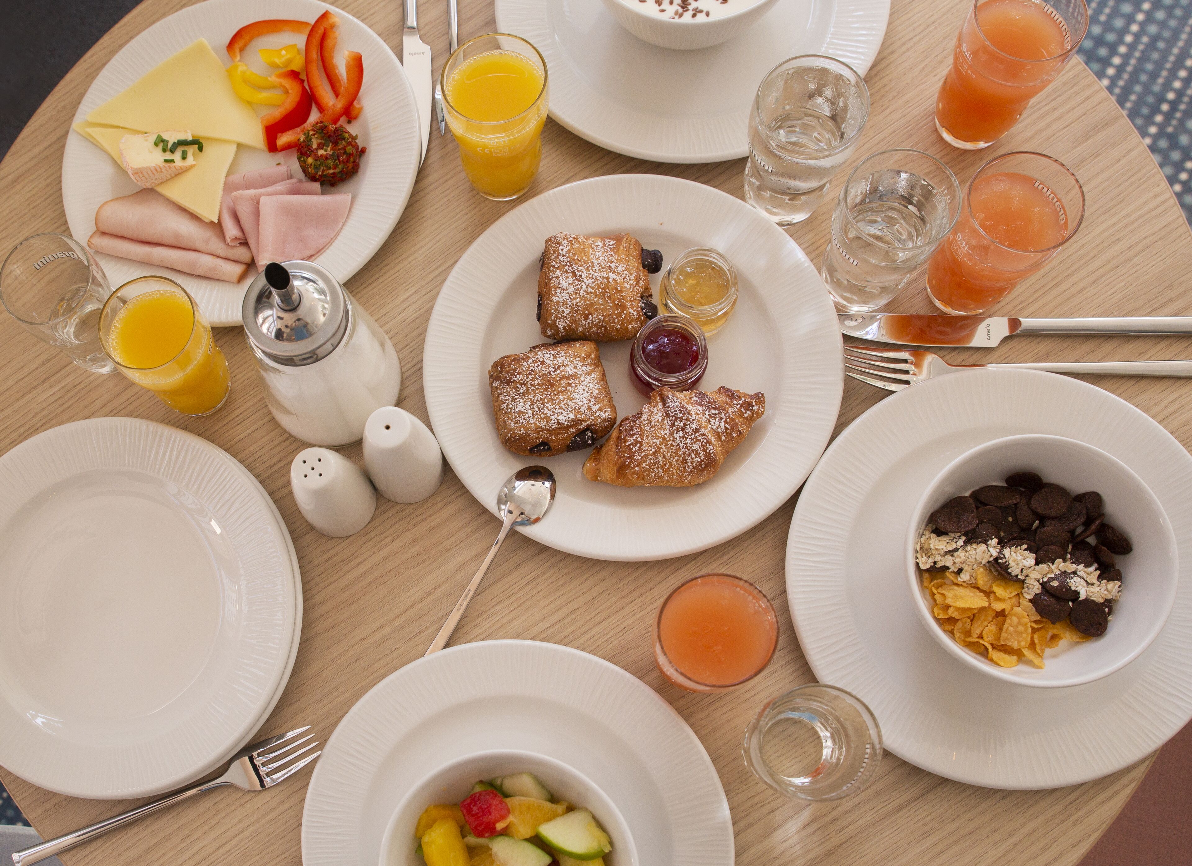 A breakfast table with plates of food, glasses of orange juice, and a bowl of cereal.