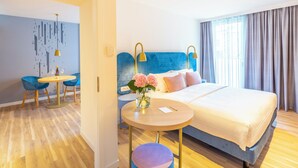 A modern hotel room with a blue headboard, a round wooden table, a blue chair, and a bed with a white bedspread. - Capri by Fraser Leipzig (Leipzig)
