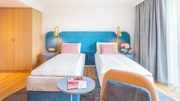 Una habitación de hotel con dos camas individuales, una mesita redonda pequeña, una silla, una mesita de noche y un armario.