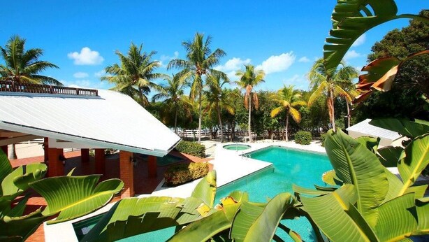 A pool area with palm trees and a building with a white roof. - Bahia Bay Resort (Key Largo)