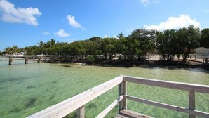 A wooden deck overlooking clear turquoise water with a backdrop of dense green foliage and a clear blue sky. - Bahia Bay Resort (Key Largo)