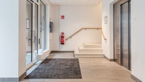 Un pasillo limpio y moderno con una puerta de cristal, un extintor, una escalera y un ascensor.
