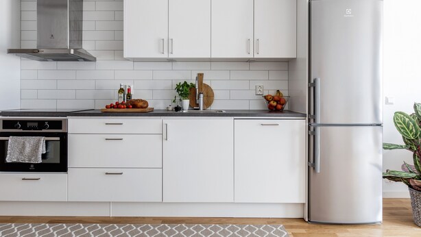 Una cocina moderna con armarios blancos, un refrigerador de acero inoxidable y un horno empotrado.