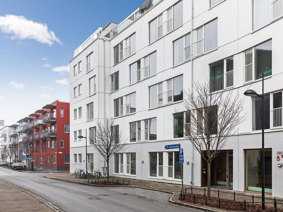 A multi-story residential building with a white facade, balconies, and a visible entrance.