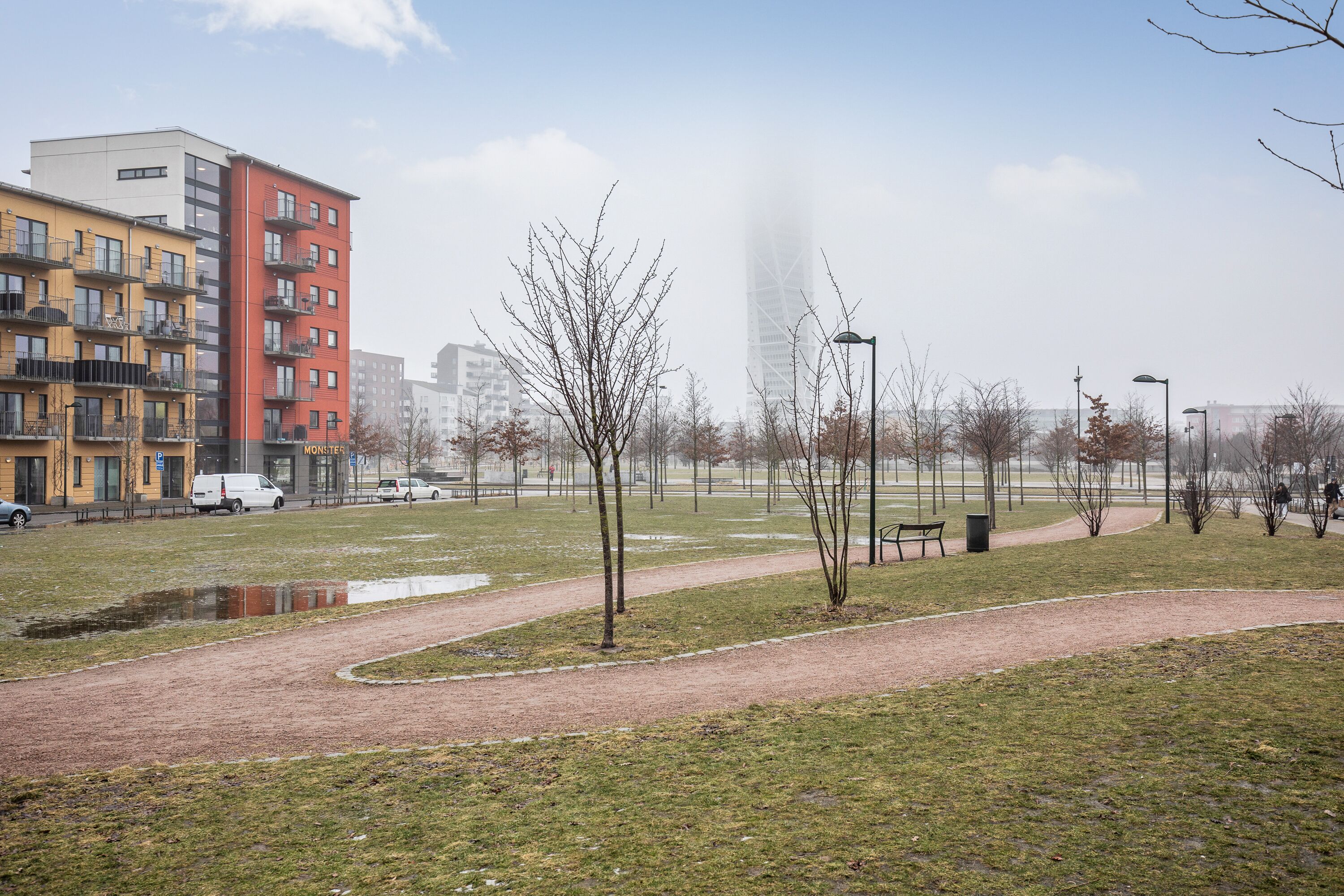 A park with a paved path, benches, and a small pond.
