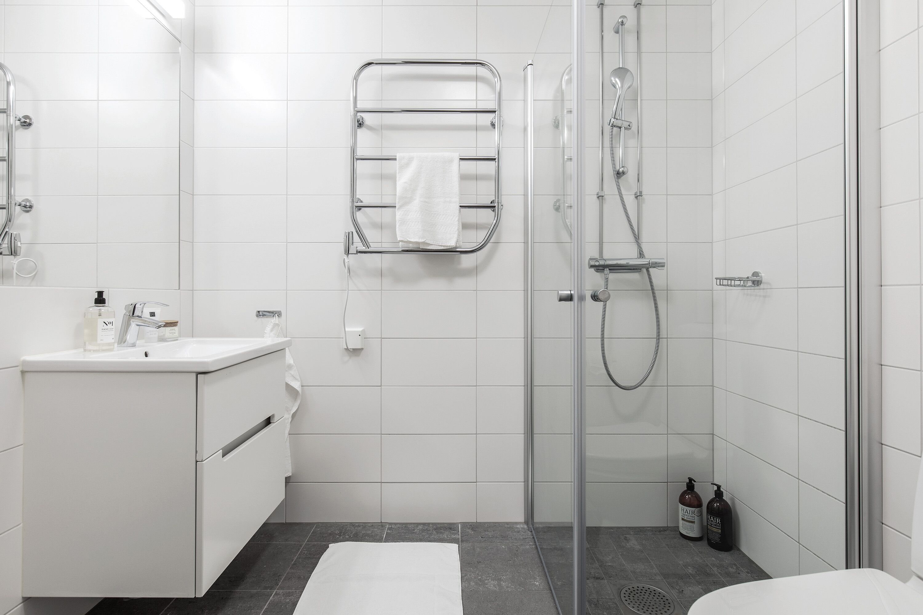 Une salle de bain moderne avec une douche à parois de verre, un lavabo blanc et un porte-serviettes.