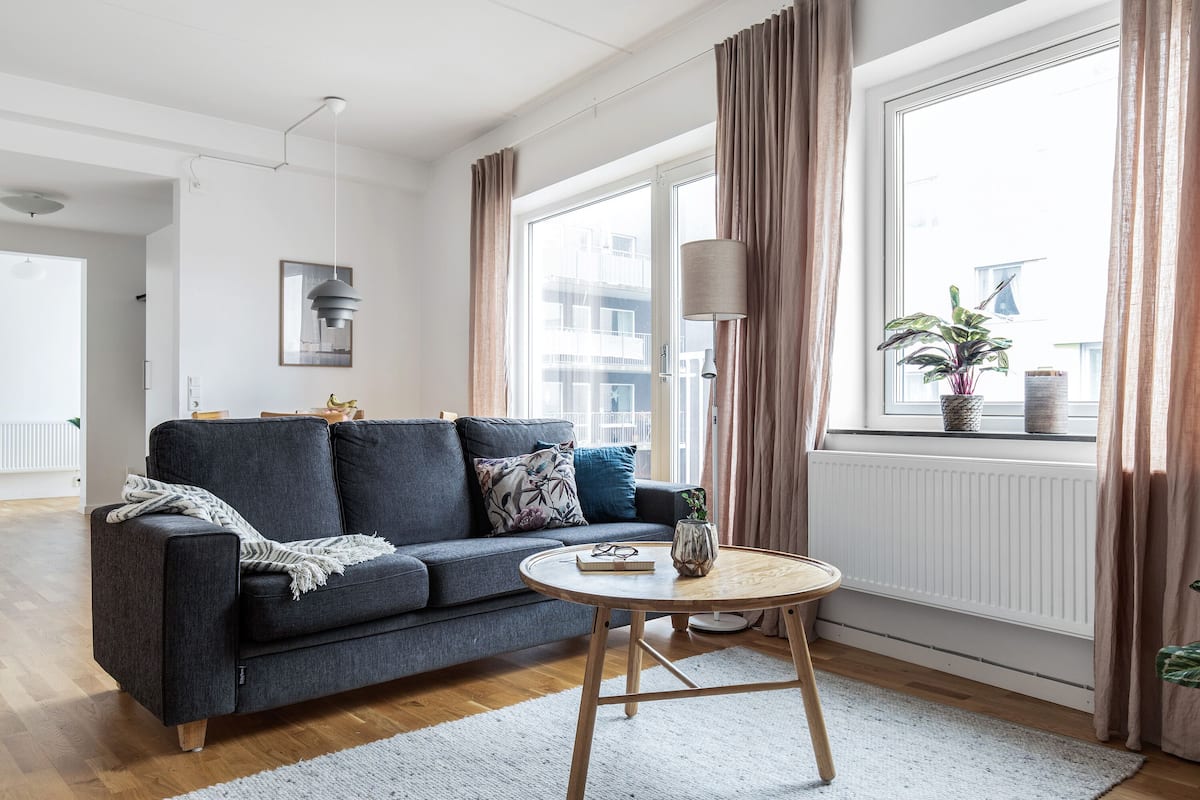 Ein modernes Wohnzimmer mit einem grauen Sofa, einem runden Couchtisch und Blick auf eine Skyline durch große Fenster.