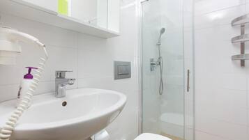 Une salle de bain avec un lavabo blanc, une douche en verre et des toilettes.