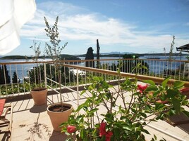 Un balcón con plantas en macetas y vista a un cuerpo de agua y terreno lejano.