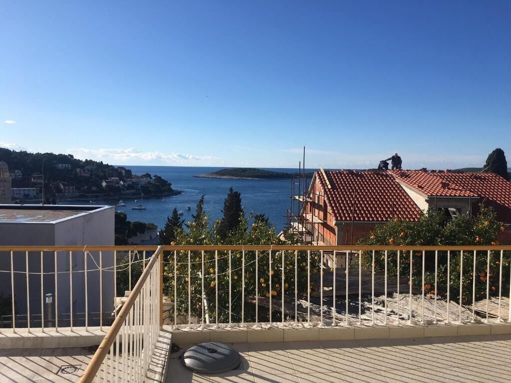 Un balcon avec vue sur la mer, un bâtiment avec un toit rouge et une île lointaine.