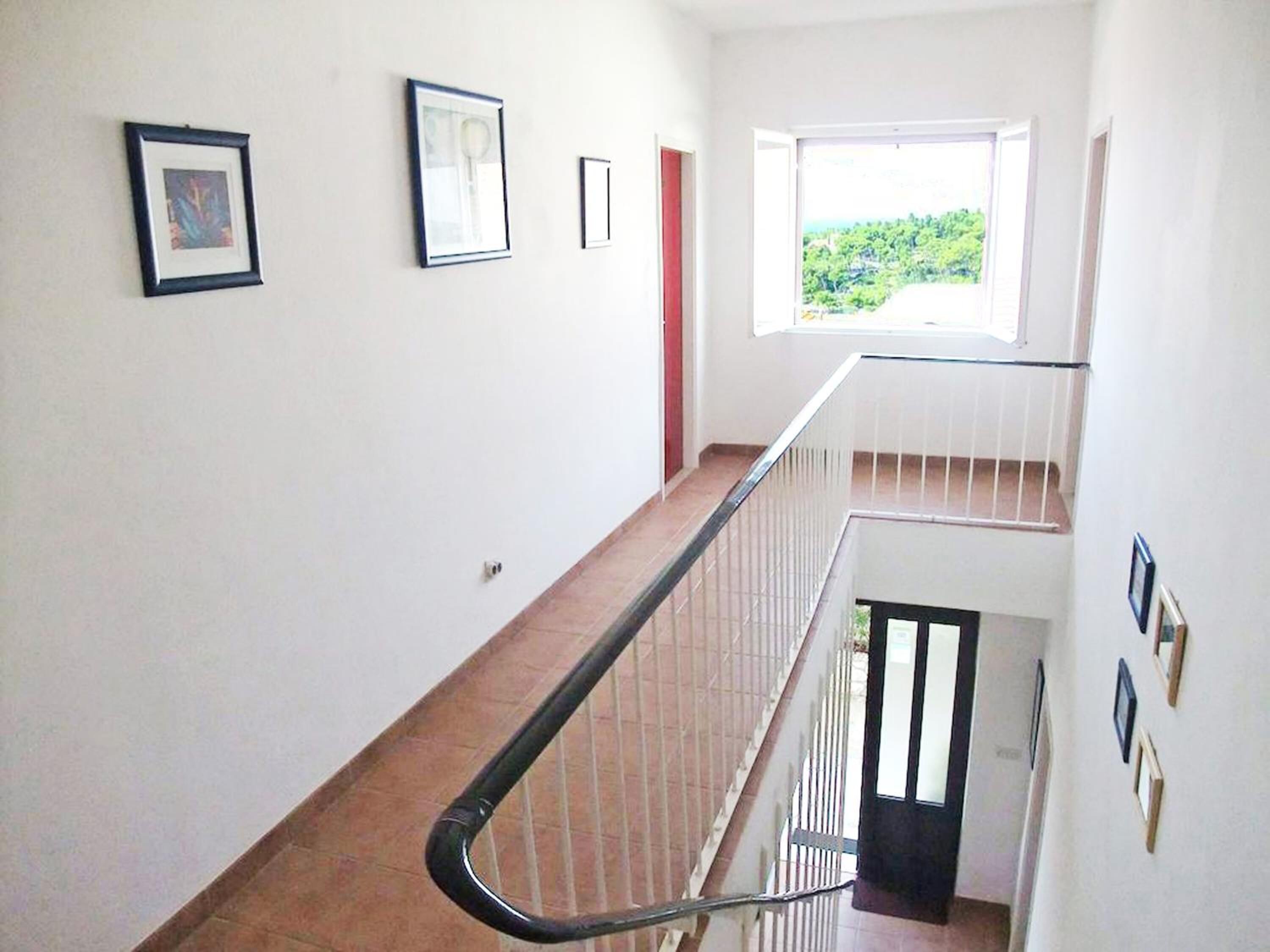 A staircase with a handrail, white walls, and framed pictures.