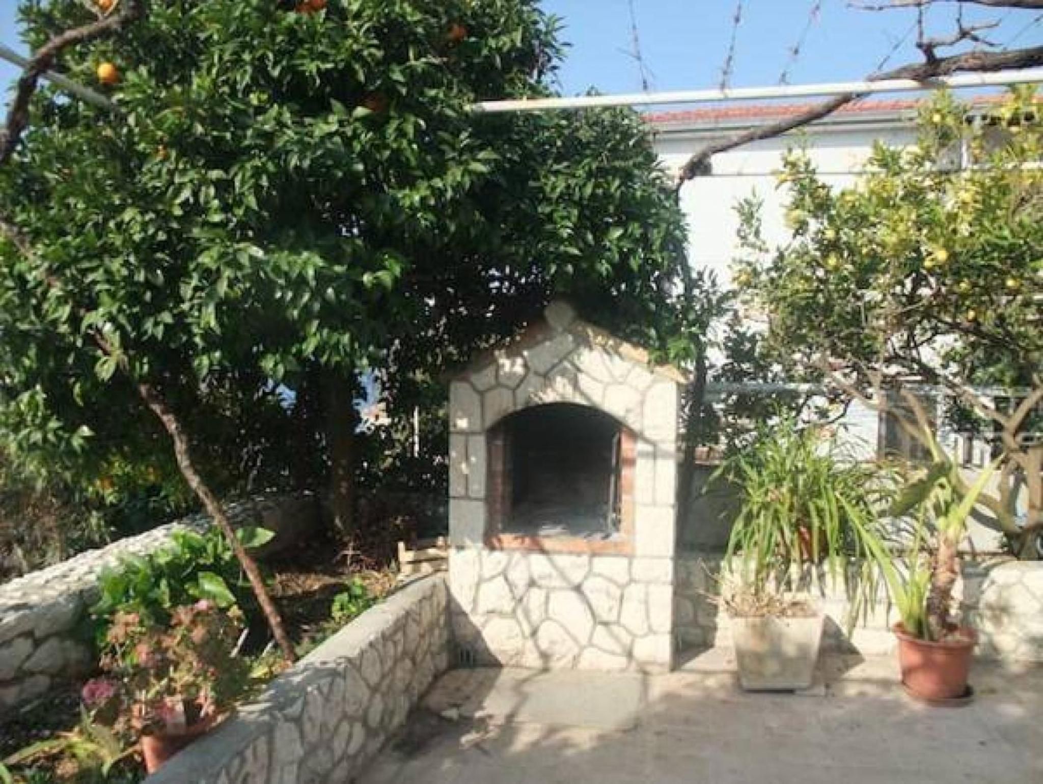 A stone-built outdoor oven structure with a stone wall and potted plants around it.