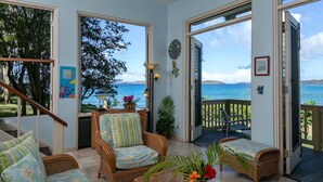 A room with wicker furniture, a view of the sea, and a balcony with a railing.
