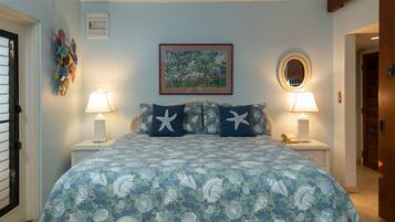 Une chambre à coucher avec un lit recouvert d’une courtepointe à motifs floraux bleus, deux tables de chevet avec des lampes, un tableau encadré au mur et un miroir au-dessus du lit.