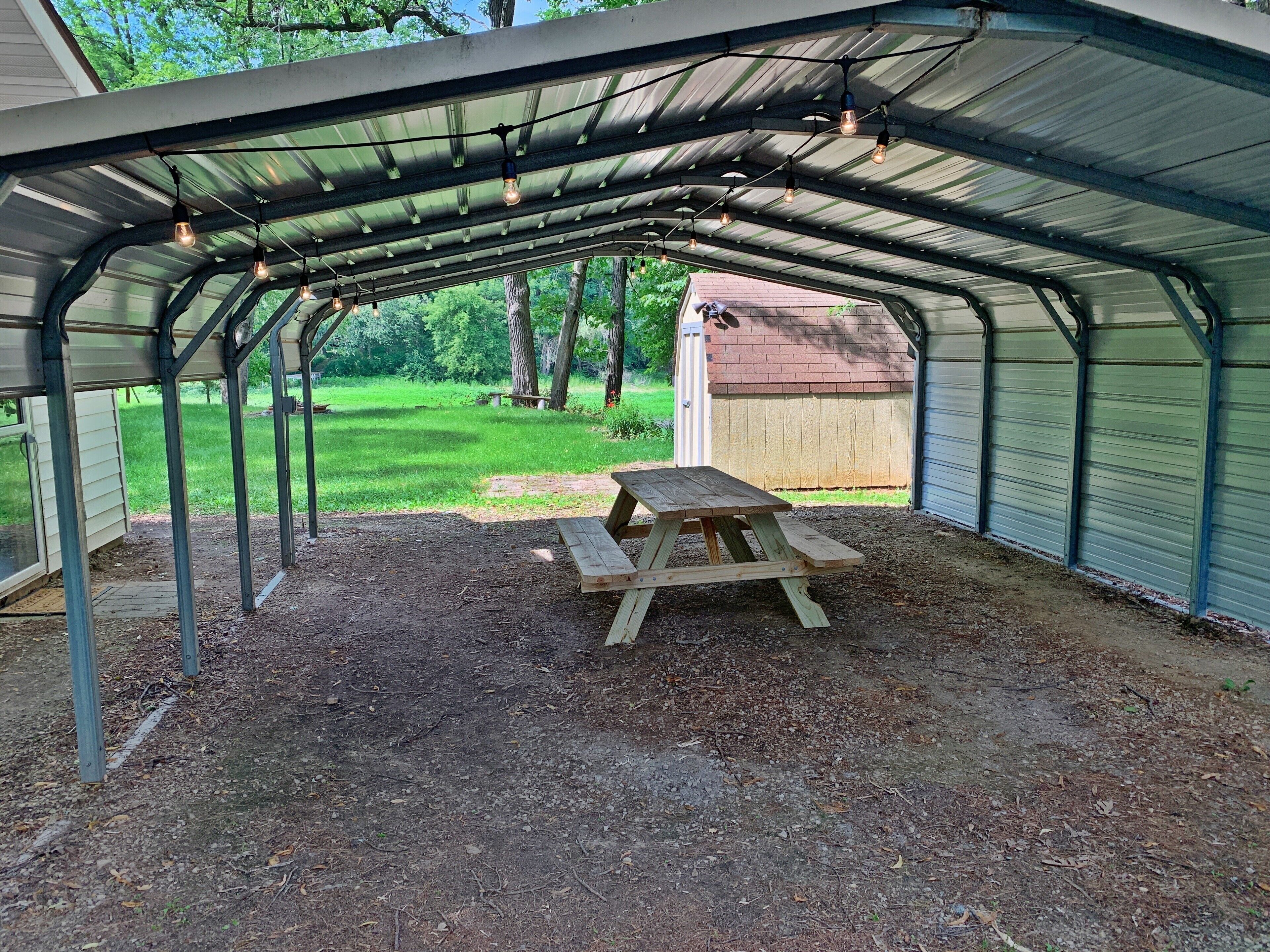 A covered outdoor area with a picnic table, metal roof, and string lights.
