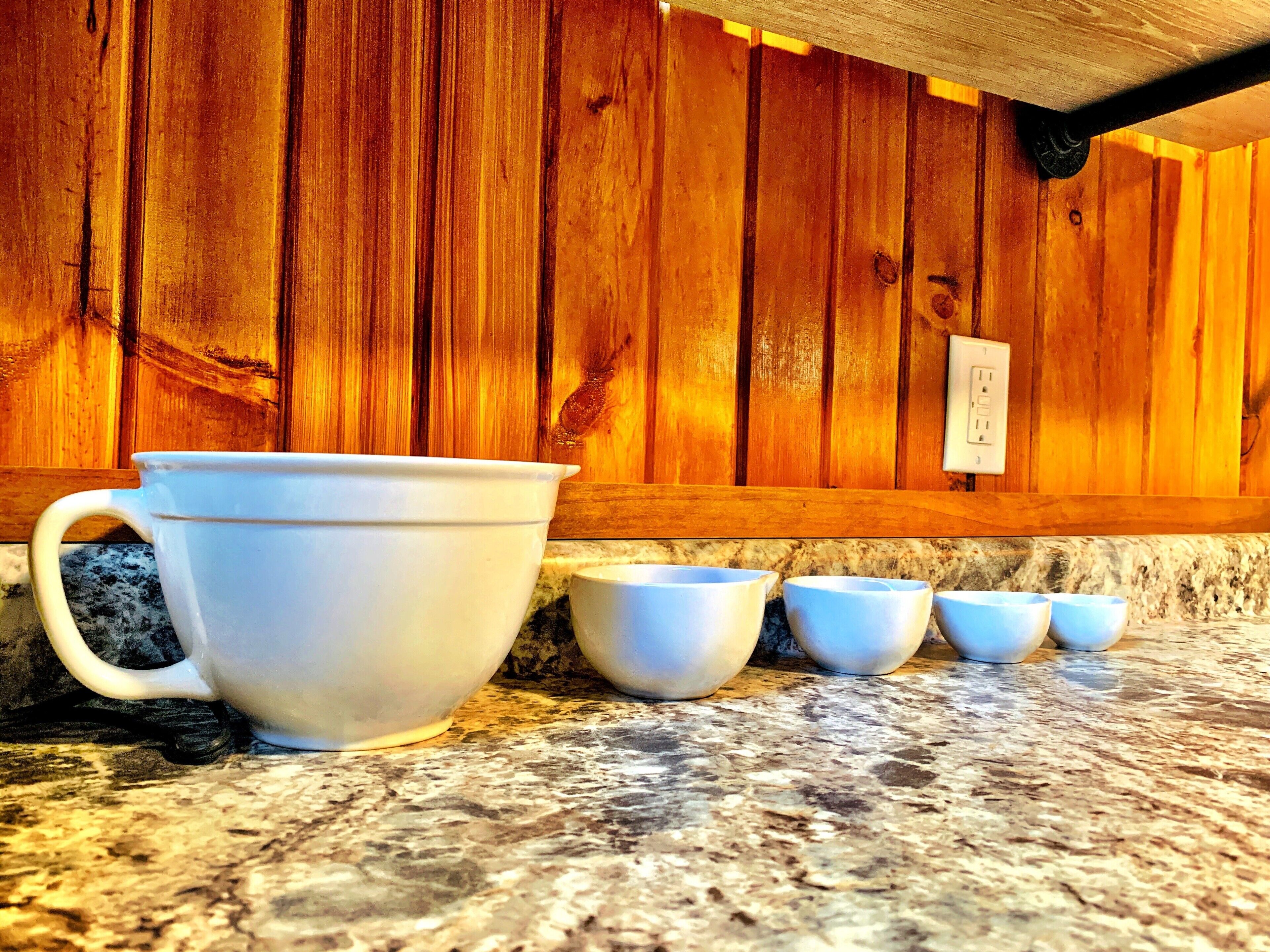 A kitchen counter with a white ceramic mug and four smaller cups.