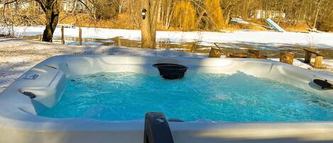 Un bain à remous installé à l’extérieur, dans un décor enneigé, avec des arbres et un ciel dégagé.