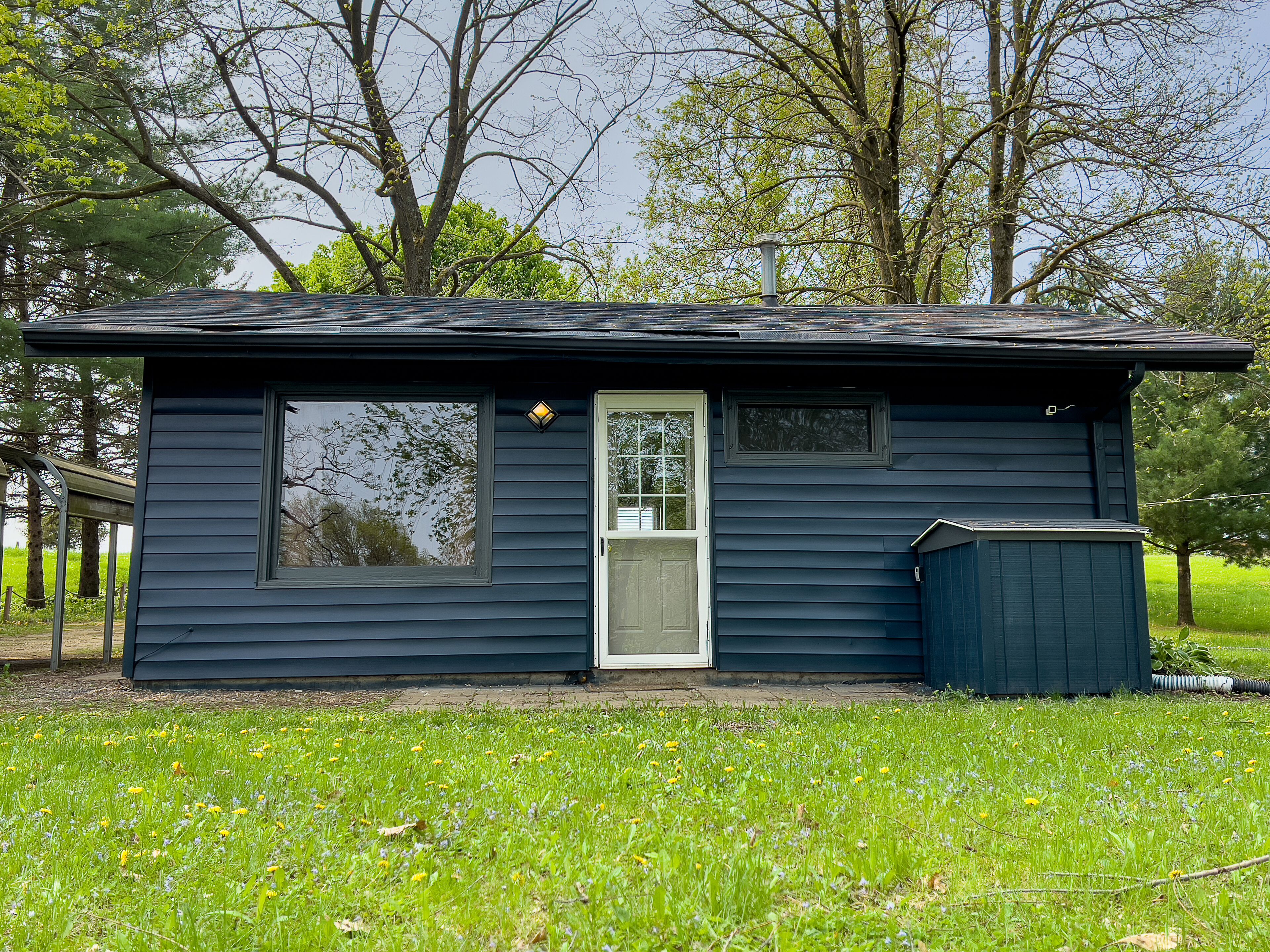 A small, single-story cabin with a front door, a window, and a small attached shed.
