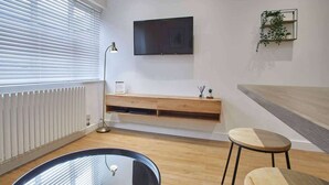 A modern living room with a round glass table, two wooden stools, a mounted TV, and a wooden bench. - Host & Stay | Routh Walk (Whitby)