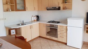 A compact kitchen with a sink, stove, oven, and a refrigerator. There are wooden cabinets and a small countertop. - Cozy Apartment Neda (Pakostane)
