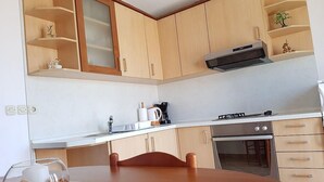 A kitchen with wooden cabinets, a countertop, a stove, and a sink. - Cozy Apartment Neda (Pakostane)