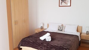 A bedroom with a bed, two bedside tables, a nightstand, a wardrobe, and a framed picture on the wall. - Cozy Apartment Neda (Pakostane)