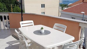 A white table and chairs on a balcony with a view of buildings and a body of water. - Cozy Apartment Neda (Pakostane)