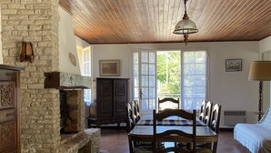 Un vaste espace dédié à la salle à manger, avec une table et des chaises en bois, une cheminée en pierre et une grande fenêtre laissant entrer la lumière naturelle.