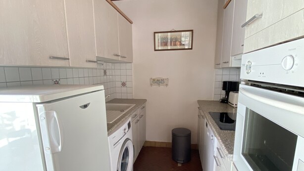 Een kleine keuken met witte apparaten, een wasmachine en een vuilnisbak.