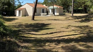 Une maison à deux étages, avec un toit recouvert de tuiles, entourée d’une pelouse et de pins.