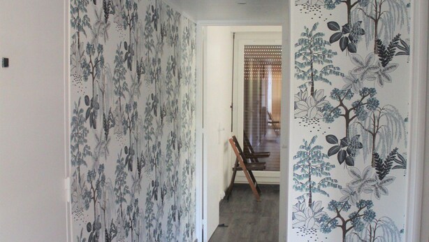 A hallway with floral wallpaper and a wooden chair in the background.