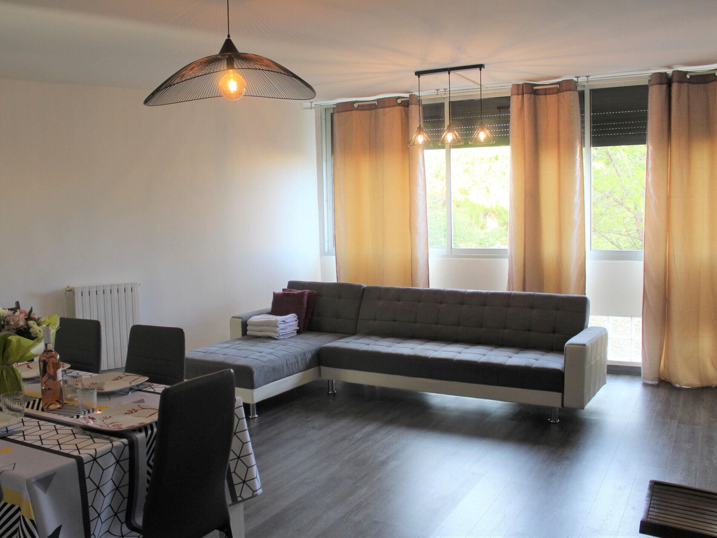 A modern living room with a sectional sofa, dining table, chairs, and large windows with curtains.
