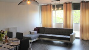 A modern living room with a sectional sofa, dining table, chairs, and large windows with curtains.