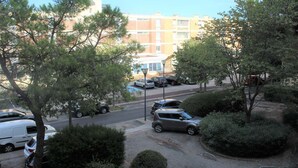 A parking lot with several cars, surrounded by trees and a building with multiple windows in the background.