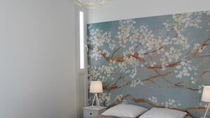 A bedroom with a bed, two bedside tables, a nightstand, and a wall painting of a tree with blossoms.