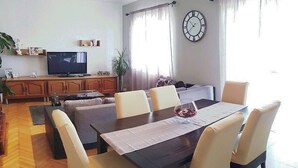 A dining area with a long table and chairs, a television on a cabinet, and a clock on the wall. - Spacious Apartment Neda (Pakostane)