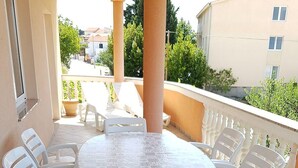 A round table with a patterned tablecloth, surrounded by white chairs on a balcony with a railing. - Spacious Apartment Neda (Pakostane)