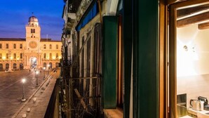 A building with a clock tower, a balcony with a metal railing, and a view of a street with street lamps. - MyPlace Piazze di Padova - Studio Balcony with view on "Piazza dei Signori" Square (Padova)