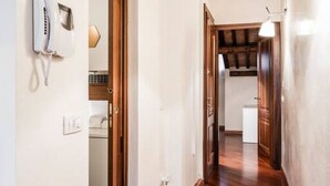 Un couloir avec un téléphone blanc fixé au mur, une porte en bois et un luminaire.