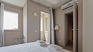 Quarto de hotel com uma cama grande, uma cadeira e uma porta aberta para outro quarto.