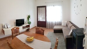 A living room with a dining table, chairs, a sofa, a TV, and a clock on the wall.