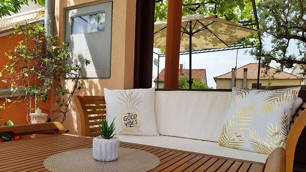 A wooden table with a woven placemat, a potted plant, and a white sofa with cushions.
