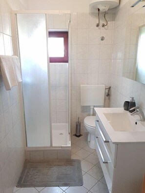 Un baño con ducha, inodoro, lavamanos y una pequeña ventana.