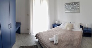 Un dormitorio con cama, mesitas de noche, un armario azul y una ventana con cortinas.