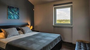 A bedroom with a bed, pillows, a nightstand, a window with a view, and a wall-mounted painting. - Villa Pomer (Medulin)