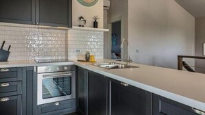 A modern kitchen with dark cabinets, a stainless steel oven, a white countertop, and a wall-mounted clock. - Villa Pomer (Medulin)