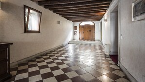 Ein Korridor mit Schachbrettboden, Holzbalken an der Decke und einer Holztür am Ende.
